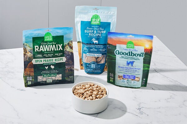 Three bags of freeze dried raw dog food sitting behind a white bowl filled with freeze dried dog food on a white marble  kitchen counter